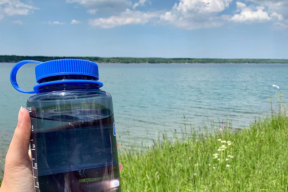 A photo, by the lake, of someone with their refillable water bottle.